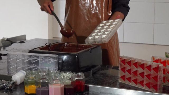 Cropped shot of a professional chocolatier wearing cooking uniform and apron working with hot melting chocolate. Confectioner making handmade chocolate candy. Profession, job concept.
