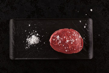 Raw meat, beef steak on black background, top view.