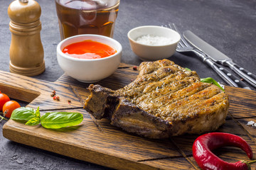 Grilled Steak on bone with knife and fork carving set on black concrete background. Selecrive focus