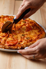 People Hands cutting homemade pizza. Hand slicing a homemade pizza with a cutter on a wooden table