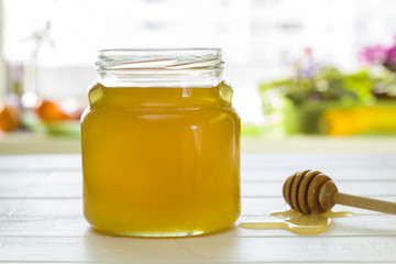 A glass jar with honey and a dipper on the kitchen table.  