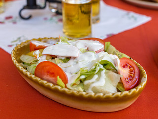 Fresh vegetable salad of tomatoes, cucumbers and lettuce leaves with yogurt sauce in oval ceramic dish. Healthy food concept. Selective focus