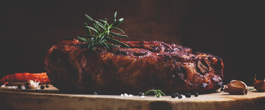 Baked pork shoulder with pepper, rosemary and garlic, vintage wooden background, selective focus and toned image