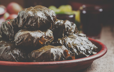 Traditional Greek dolma with meat in grape leaves, yogurt sauce, grapes and red wine on a clay dish, selective focus and toned image
