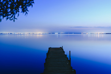 Fototapeta premium Pier on a lake at sunset with calm water and reflections of relaxing lights.