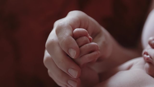 Young mother gently stroking the hands of her newborn baby