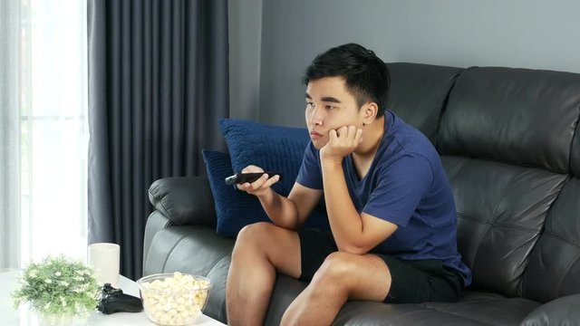 4k of young bored man watching tv and sitting on sofa in the living room