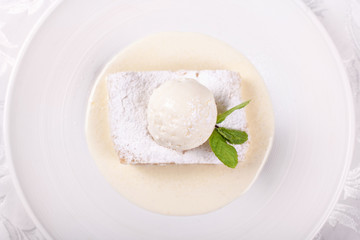 Fruit apple strudel cake served with ice cream, mint leaf and vanilla sauce. Classical austrian dessert on white plate. Sweet dessert in the restaurant. Morning light.