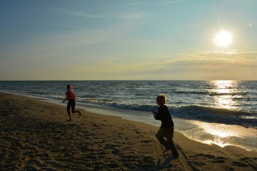 Zwei Kinder rennen beim Sonnenuntergang am Strand , mit Sonne über dem Meer