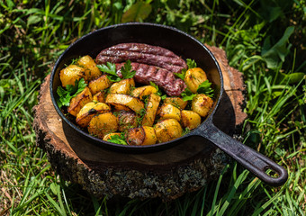 Fried potatoes with meat sausages in a cast-iron frying pan