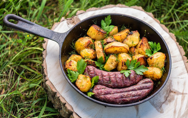 Fried potatoes with meat sausages in a cast-iron frying pan