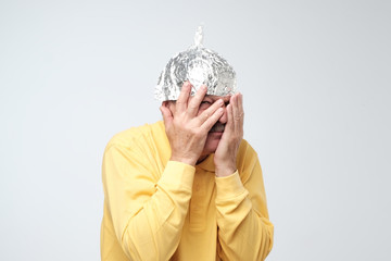 Caucasian mature man in a tin foil hat displeased closing his face with hands.