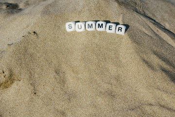 Summer concept made with dice with letters on the wet sand of a beach and marine motives.
