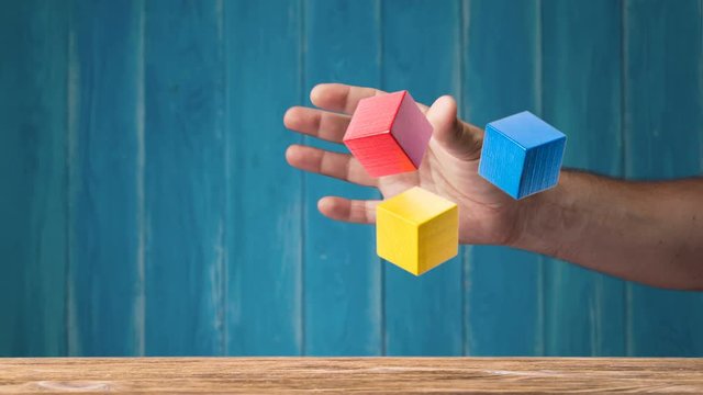 Male hand is juggling colorful wooden cubes, stop motion. Concept of creative, logical thinking. Floating shapes.