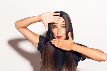 Fototapeta premium Young adult woman framing her face with her hands, making funny faces. In studio over a white background.
