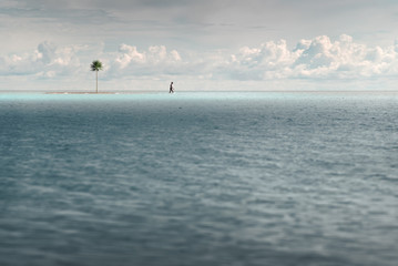 A man walks in shallow turquoise water. Near a small uninhabited island