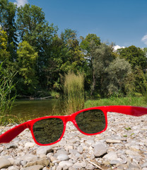 Blick durch eine rote Sonnenbrille am Ufer der Isar in München