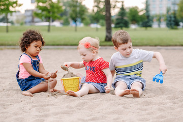 Portrait of three cute Caucasian and hispanic latin toddlers babies children sitting in sandbox...