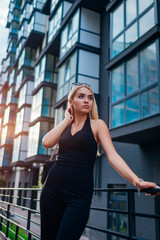 Beauty fashion model wearing formal black clothing and accessories outdoors. Blonde young girl walking on city street