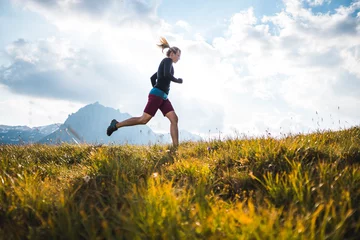 Sportliches Mädchen, das auf einem Pfad durch eine wunderschöne Bergwiese in den österreichischen Alpen läuft © Daniel J