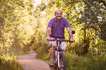 Joyful senior man riding a bike in a park on a beautiful sunny day