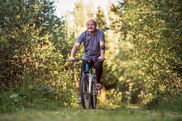 Fototapeta na wymiar Joyful senior man riding a bike in a park on a beautiful sunny day