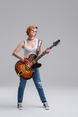 Young woman musician with an acoustic guitar in hand on a gray background. He laughs and plays rock...