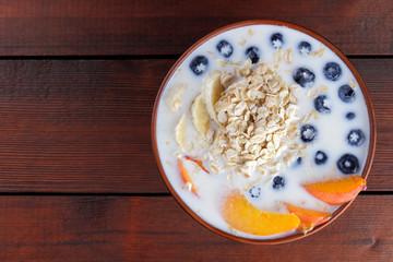 Oatmeal porridge with milk and fruit on a wooden background, healthy porridge with pieces of banana and peach, breakfast with fiber, calcium and vitamins, food for the schoolboy