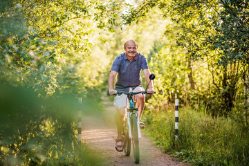 Joyful senior man riding a bike in a park on a beautiful sunny day