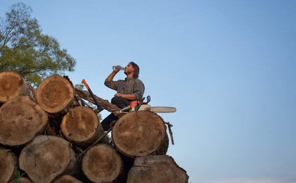 Lumberjack resting and drinking water on pile of logs