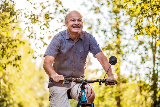 Joyful senior man riding a bike in a park on a beautiful sunny day