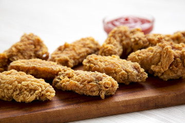 Chicken wings on a wooden board with red pepper sauce on white wooden table, closeup. Selective focus.