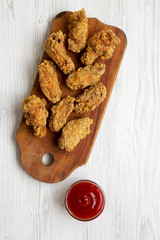 Flat lay of chicken wings on a wooden board with red pepper sauce on white wooden table. Top view, overhead, from above.