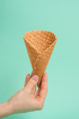 Female hand with waffle cone on mint background