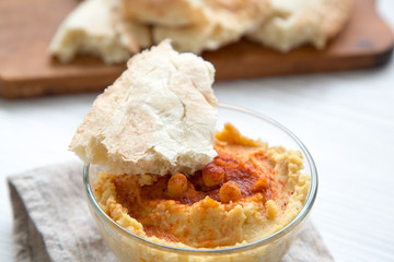 Hummus in bowl with roasted chickpeas, paprika, olive oil and pita bread, closeup.