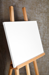 pure white synthetic canvas stretched on a wooden stretcher standing on a wooden easel for artists. On sackcloth fabric texture background. Art, creativity, hobby, job and creative occupation concept