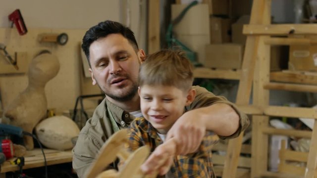 Medium shot of happy father and son playing with wooden airplane toy in carpentry workshop