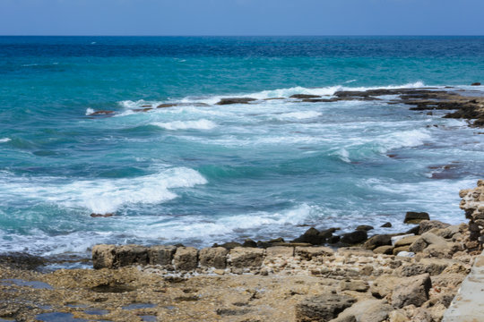Fototapeta sea waves run on the rocky shore with the ruins of ancient buildings