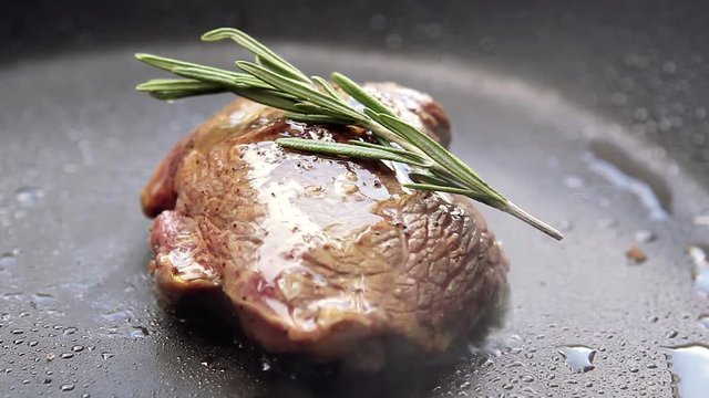 Cooking raw steak with oil and rosemary