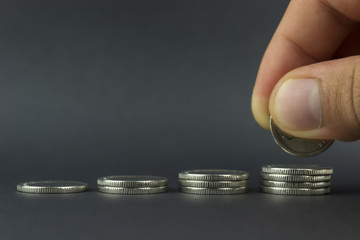 copy spaсe,  hand puts coins, in a row in ascending order,  against a dark background