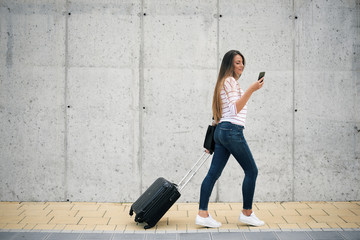 Woman carrying luggage and using smart phone while walking to the station.