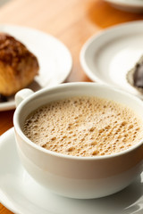 Close up on coffee in a white cup and saucer,  with pastry in the background