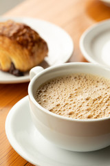 Close up on coffee in a white cup and saucer,  with croissant in the background