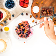 Top view showing hands eating porridge with honey nuts, blueberries on white wooden table selective focus, blurred background Good morning - healthy breakfast background
