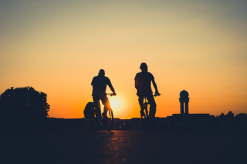 Fototapeta na wymiar silhouette of two people riding bicycle with sunset sky background