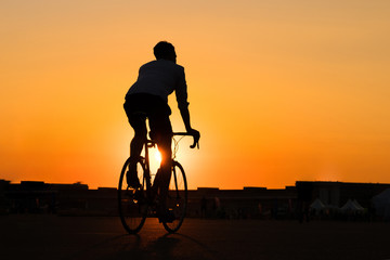 Fototapeta na wymiar silhouette of young man riding racing bicycle with sunset sky background