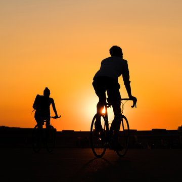 silhouette of couple riding  bicycle with sunset sky background