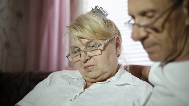 an elderly couple looks at their photos sitting at home on the couch. husband and wife with glasses watching his album.
