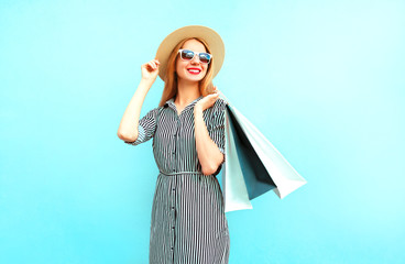 Fashion smiling woman with shopping bags in striped dress, round straw hat on blue background