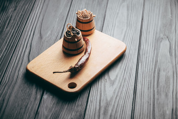 Spices: black pepper, red pepper, chili lie on a brown wooden board on a black table. Place under the text.